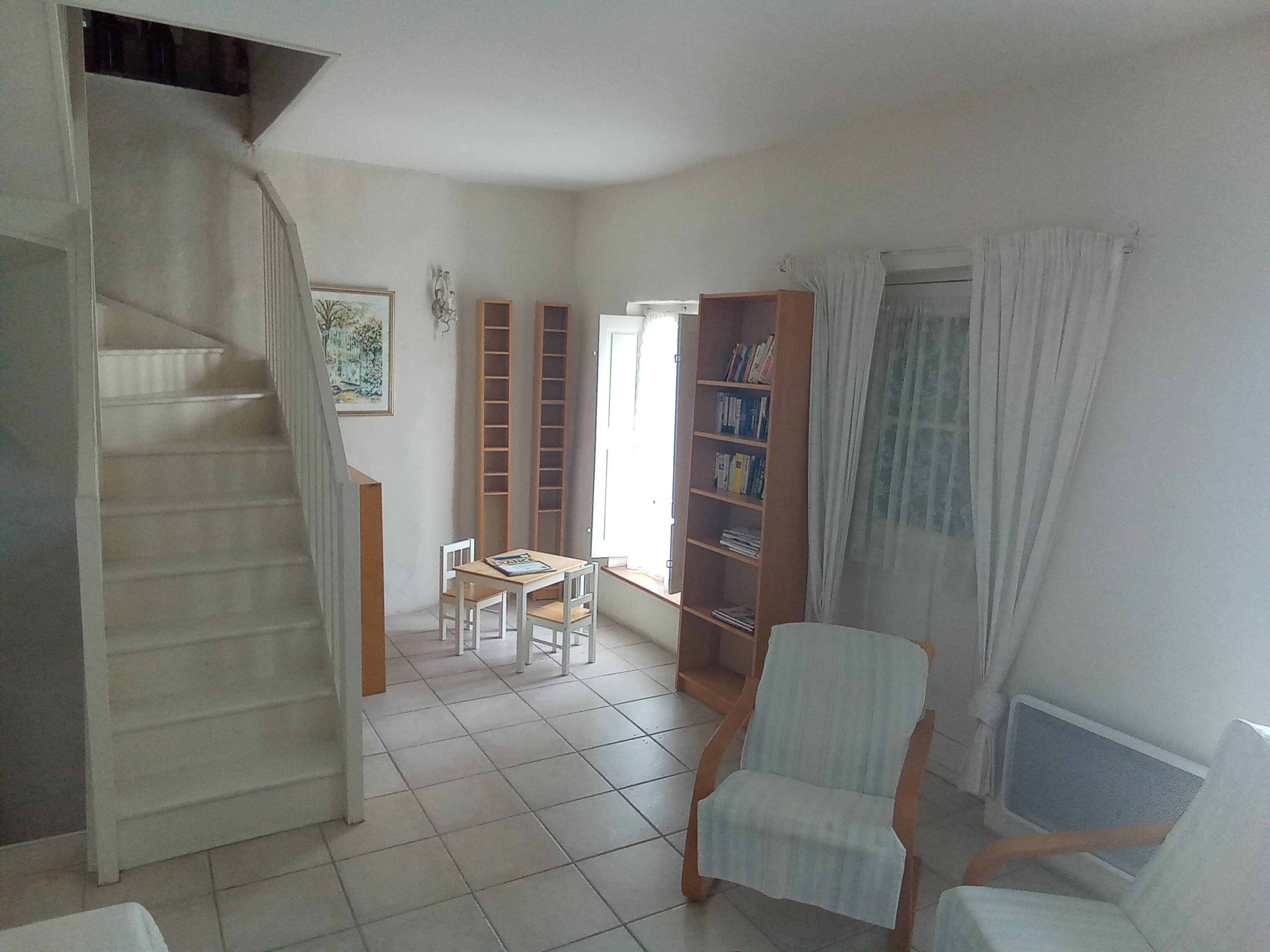 Amplia sala de estar con escalera, estantería, una silla y un radiador.