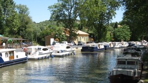A canal lined with boats, a building with a sloped roof, and trees in the background. - Grand old Villa with pool in the heart  of  Capestang town (on the Canal du Midi) (Capestang)