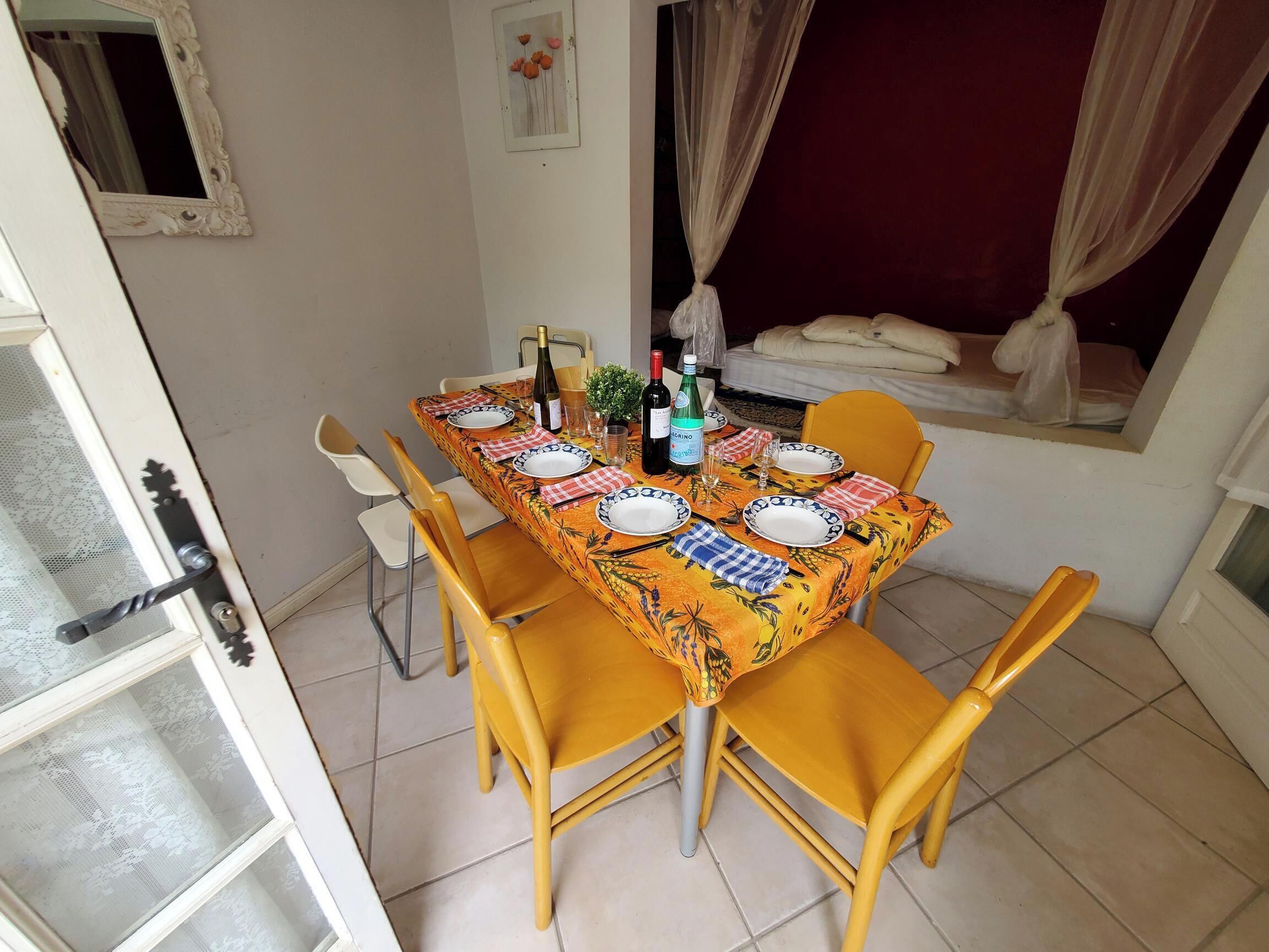 A dining area with a table set for four, chairs, a window with curtains, and a door with a metal handle.