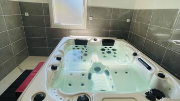 Uma banheira de hidromassagem num banheiro com azulejos escuros e uma pequena janela acima.