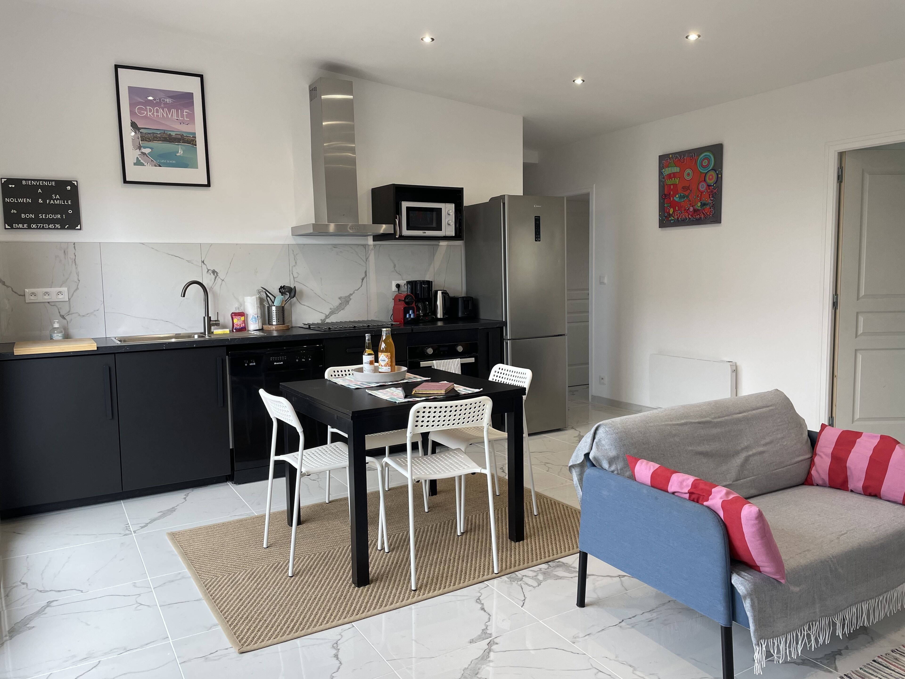 A modern kitchen with a dining area, a sofa, and a painting on the wall.