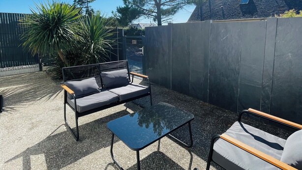 Ein Sitzbereich im Freien mit einer Couch, Stühlen und einem Tisch, umgeben von Kies und einem Holzzaun.