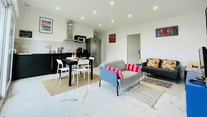 Ein modernes Wohnzimmer mit einer Couch, einem Esstisch mit Stühlen, einer Küchenzeile inklusive Mikrowelle und Herd sowie einer Tür zu einem weiteren Raum.
