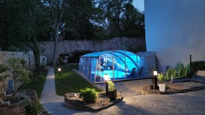 Una piscina cubierta con paredes de vidrio, junto a un jacuzzi, rodeada de un muro de piedra y vegetación.