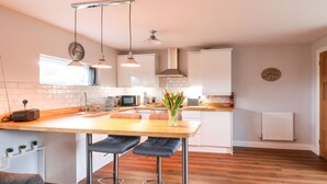 A modern kitchen with a wooden countertop, two bar stools, pendant lights, a microwave, and a toaster.