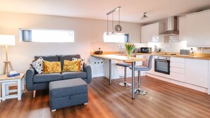 A modern kitchen with a dining area, a sofa, and a small table with a lamp.