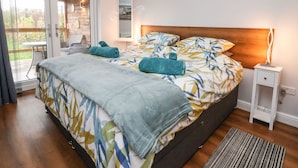 A bedroom with a large bed, a nightstand, a mirror, and a view of the outdoors through a sliding door.