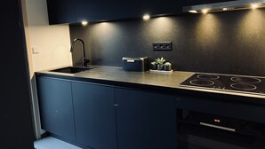 A modern kitchen with dark cabinetry, a black countertop, a built-in stove, and under-cabinet lighting.