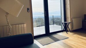 A modern living room with a large sliding glass door leading to a balcony with a view of the sea.