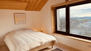 A bedroom with a wooden bed, a window with a view of a town, and a motivational quote on the wall.
