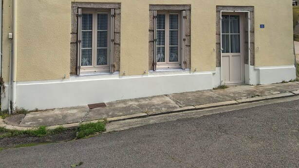 Un edificio a due piani con tetto in tegole, un camino e un piccolo portico con una porta.