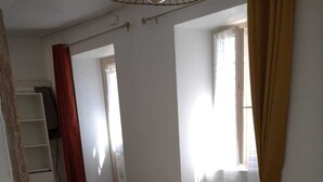 Una stanza con pavimento in legno, una panca, un tavolo, uno scaffale e una finestra con tende.