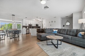 Ein modernes Wohnzimmer mit einem grauen Ecksofa, einem Holztisch und einem Essbereich mit Tisch und Stühlen.