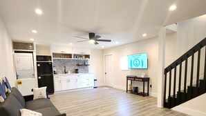 A modern living room with a grey sofa, a ceiling fan, and a kitchen in the background. - #79 The Summer Loft by Joyful Moments Vacations (Clearwater)