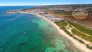 Vue aérienne d’une ville côtière avec une plage, des eaux cristallines et des immeubles résidentiels.