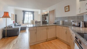 A modern kitchen with granite countertops, a built-in oven, and a dining area with a table and chairs. - Large & Central 2BD Flat - Tower Hill (London)