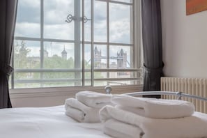 A hotel room with a bed, a window with a view of a bridge and buildings, and a radiator. - Large & Central 2BD Flat - Tower Hill (London)