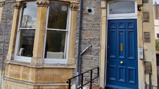 Un edificio de varios pisos con fachada de piedra y enlucido, una puerta azul y una pequeña escalera de ladrillo que conduce a la entrada.