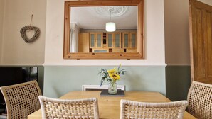 Un comedor con una mesa de madera, sillas de mimbre, un jarrón con flores y un espejo sobre la mesa.