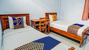 Quarto de hotel com duas camas de solteiro, cada uma com cabeceira de madeira e roupa de cama branca. Há uma mesa de madeira e uma cadeira no quarto.