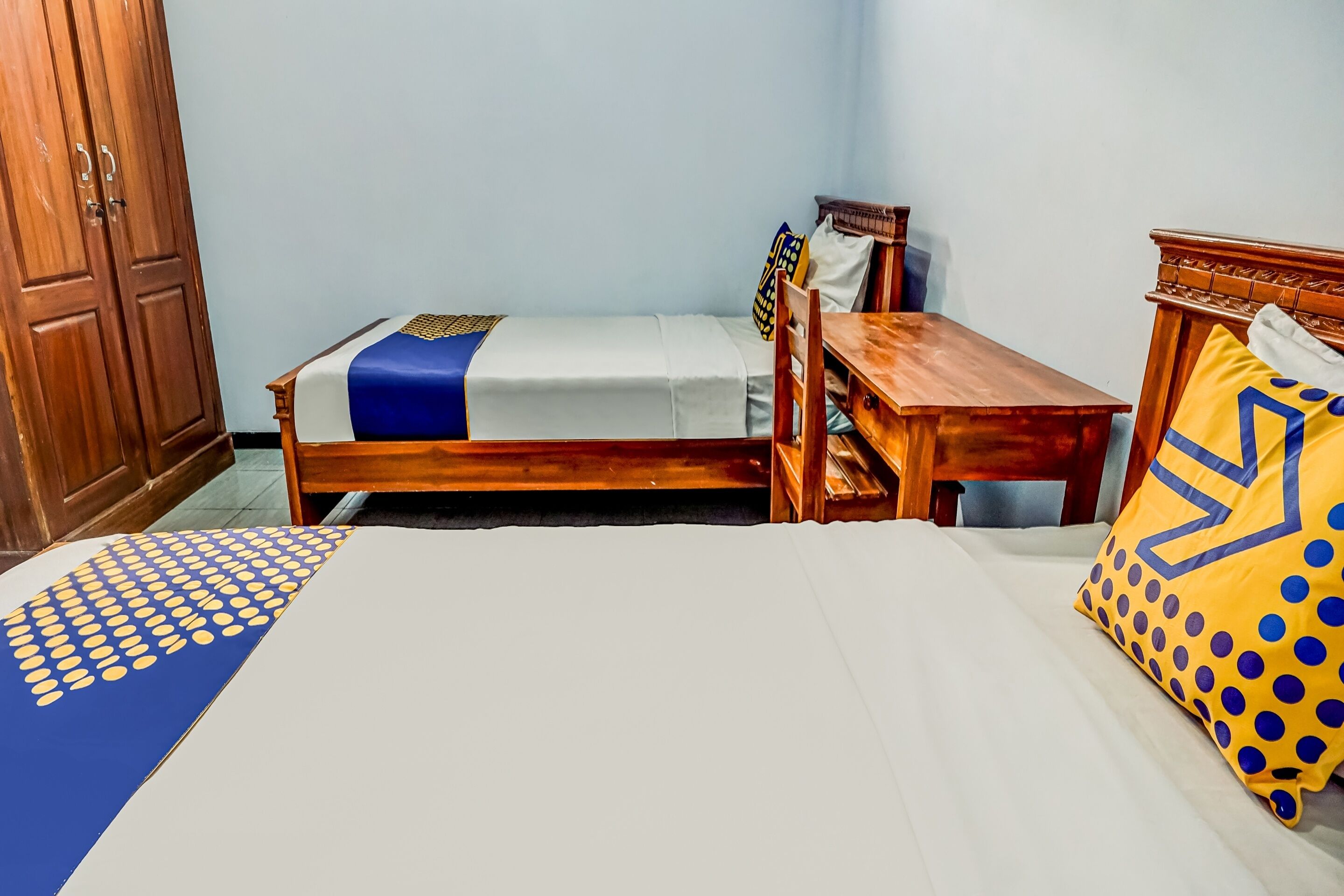 Un dormitorio con una cama individual, una mesita de noche de madera, un armario de madera y una pequeña mesa de madera.