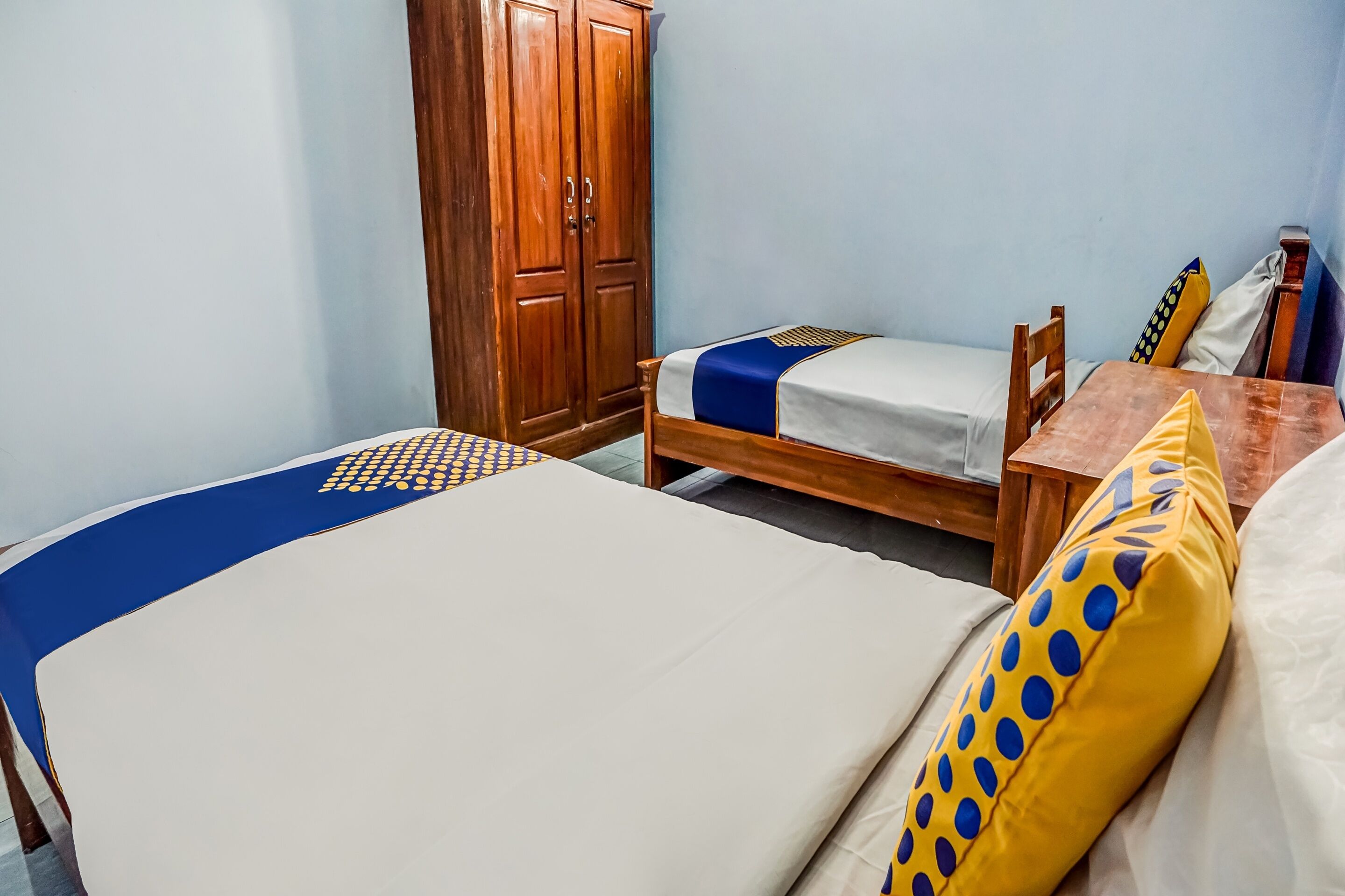 A room with two beds, a wooden wardrobe, and a small table.