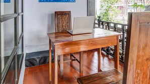Uma mesa de madeira com um laptop e um ornamento decorativo, um chão de azulejos e uma varanda com guarda-corpo.