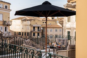 A balcony with wicker furniture, a table with wine glasses, and a black umbrella. - Penthouse Suite Sea View (Corfu)