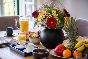 A breakfast setting with a fruit bowl, a pitcher of orange juice, a vase of flowers, and a pineapple on the table. - Penthouse Suite Sea View (Corfu)