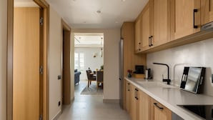 A modern kitchen with wooden cabinets, a stainless steel refrigerator, and a white countertop. - Penthouse Suite Sea View (Corfu)