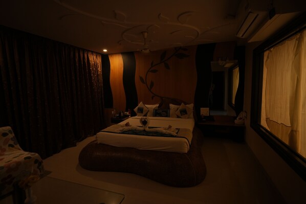 A dimly lit hotel room with a bed, a sofa, and a large window with curtains. - Hotel City Symphony (Nanded)