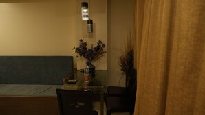 Una habitació poc il·luminada amb una taula de menjador, cadires, un ram de flors i un sofà.