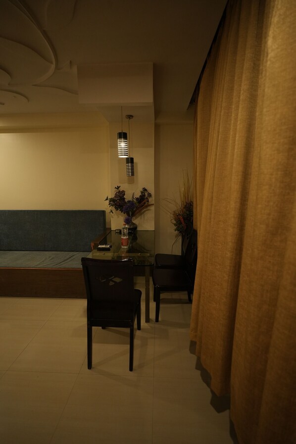 A dimly lit room with a dining table, chairs, a vase with flowers, and a sofa. - Hotel City Symphony (Nanded)