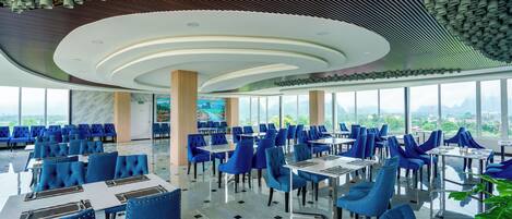 A modern restaurant with blue upholstered chairs and tables, large windows offering a city view, and a unique ceiling design with cylindrical elements.