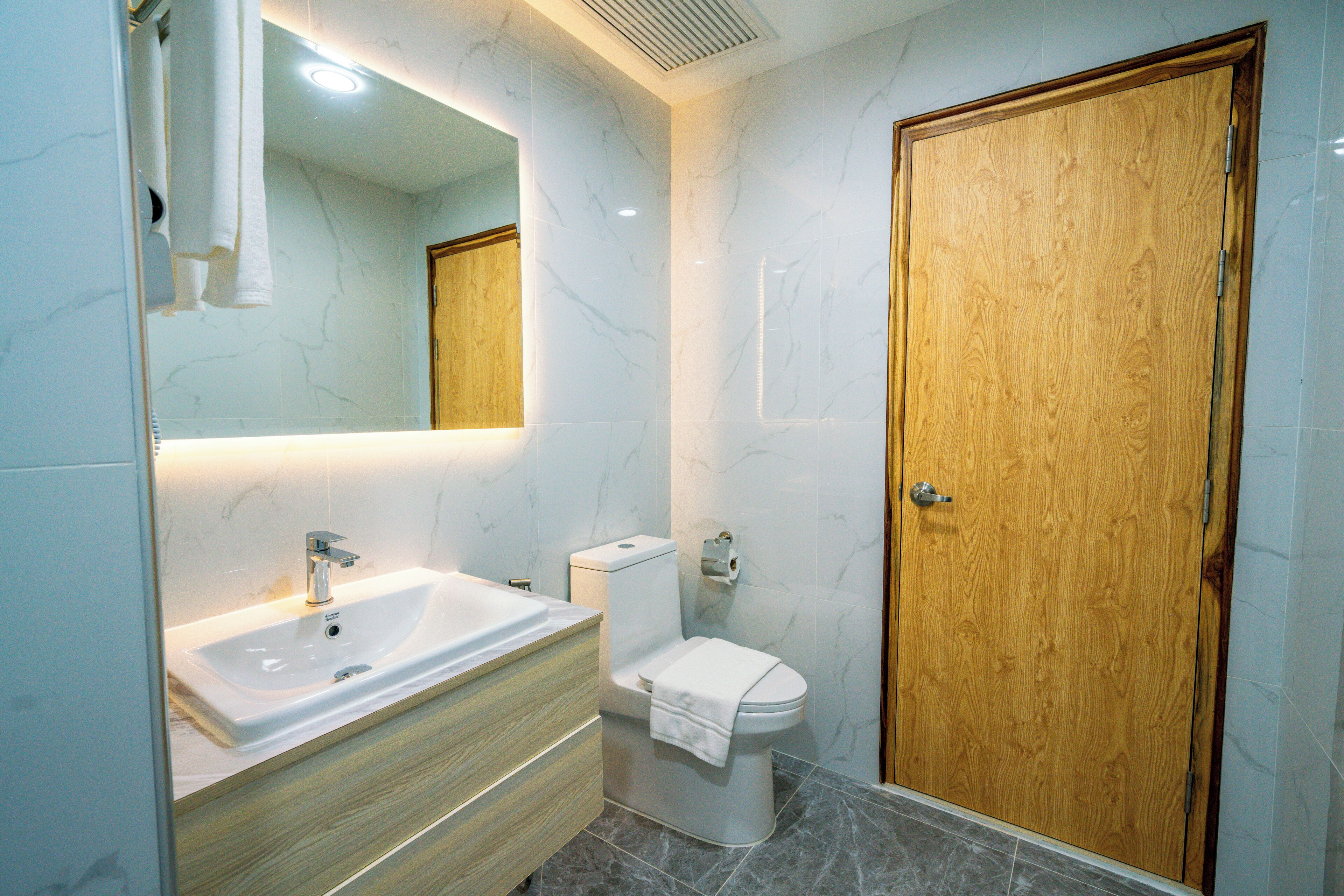 A bathroom with a white sink, wooden vanity, a toilet, and a wooden door.