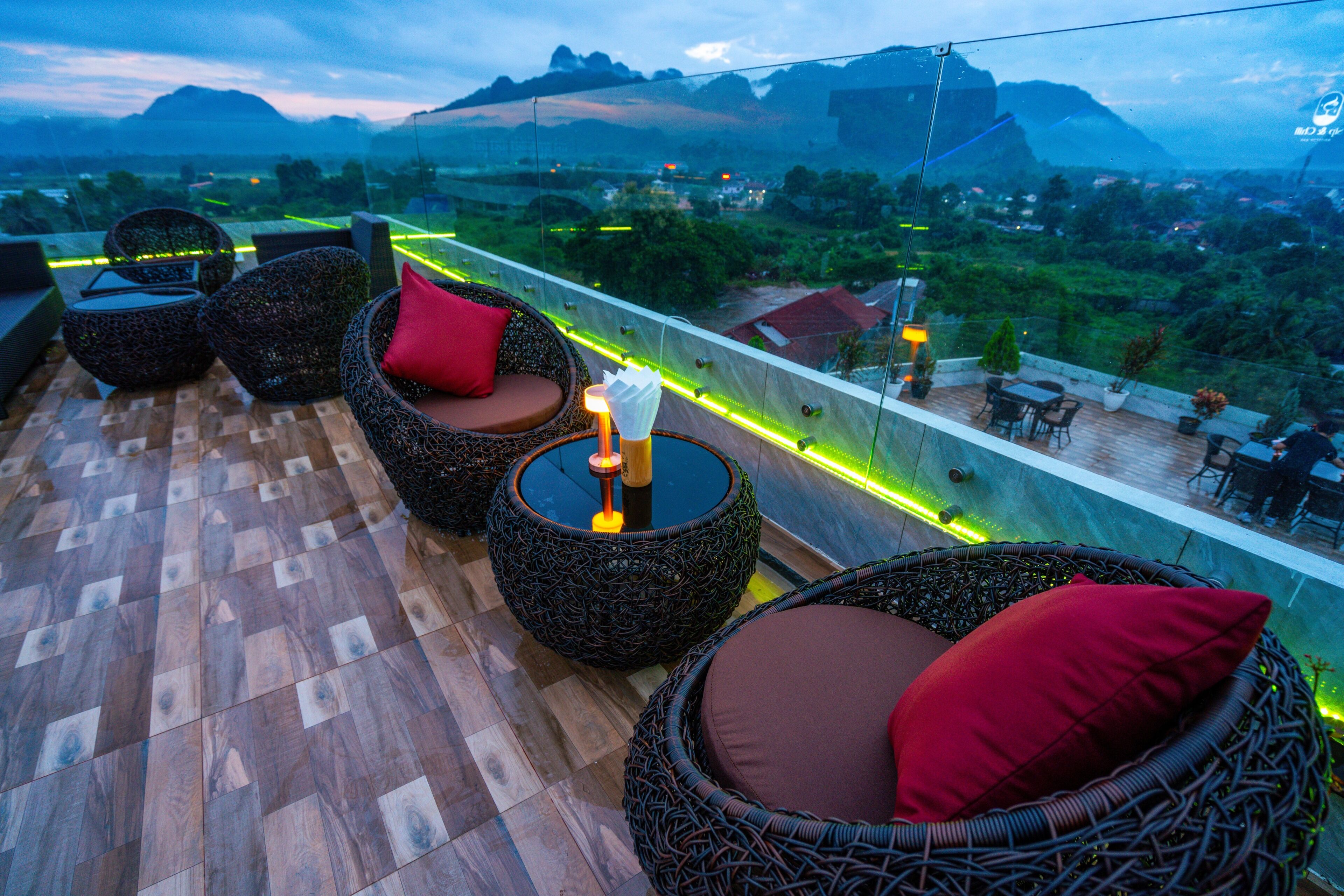 Eine Dachterrasse mit Korbmöbeln, Blick auf die Landschaft und einer Glasreling.