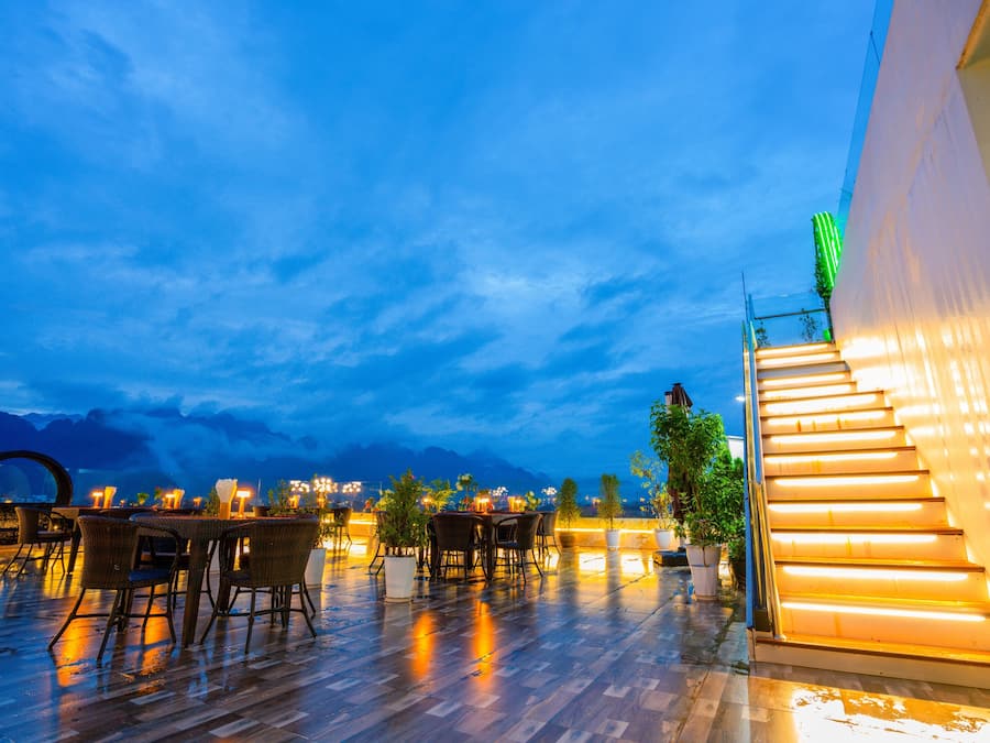 An outdoor dining area with tables and chairs, a staircase with illuminated steps, and a view of the mountains in the background.
