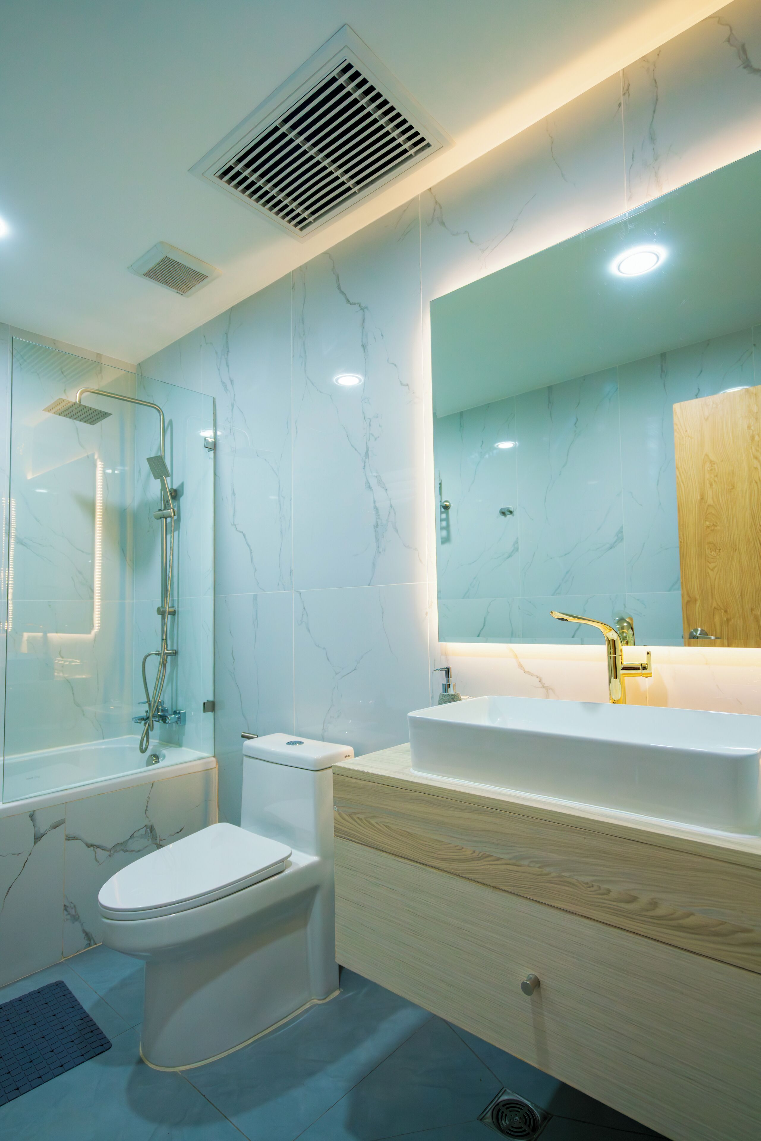 Un baño moderno con ducha envuelta en vidrio, inodoro blanco y tocador con un espejo grande.