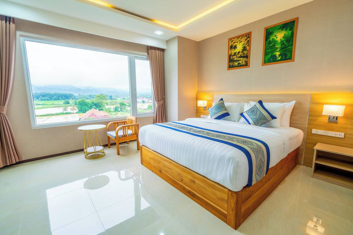 Ein Hotelzimmer mit einem großen Bett, einem kleinen runden Tisch und Blick ins Freie.