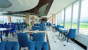 Un restaurant spacieux avec des chaises et des tables recouvertes d’un tissu bleu, de grandes fenêtres offrant une vue sur l’extérieur et un design moderne au niveau du plafond.