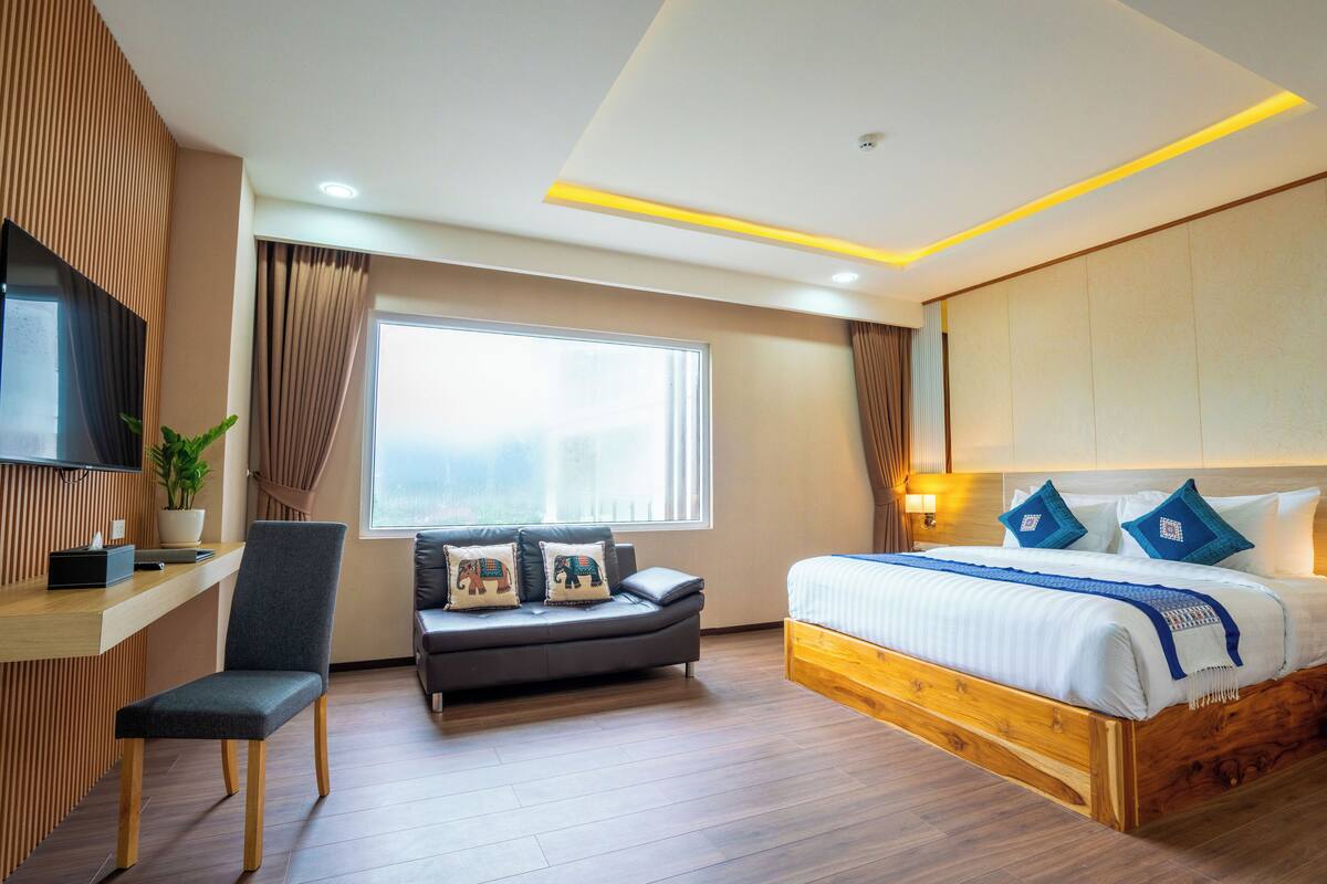 Ein modernes Hotelzimmer mit einem hölzernen Bett, einer Couch, einem Schreibtisch und einem Fernseher.