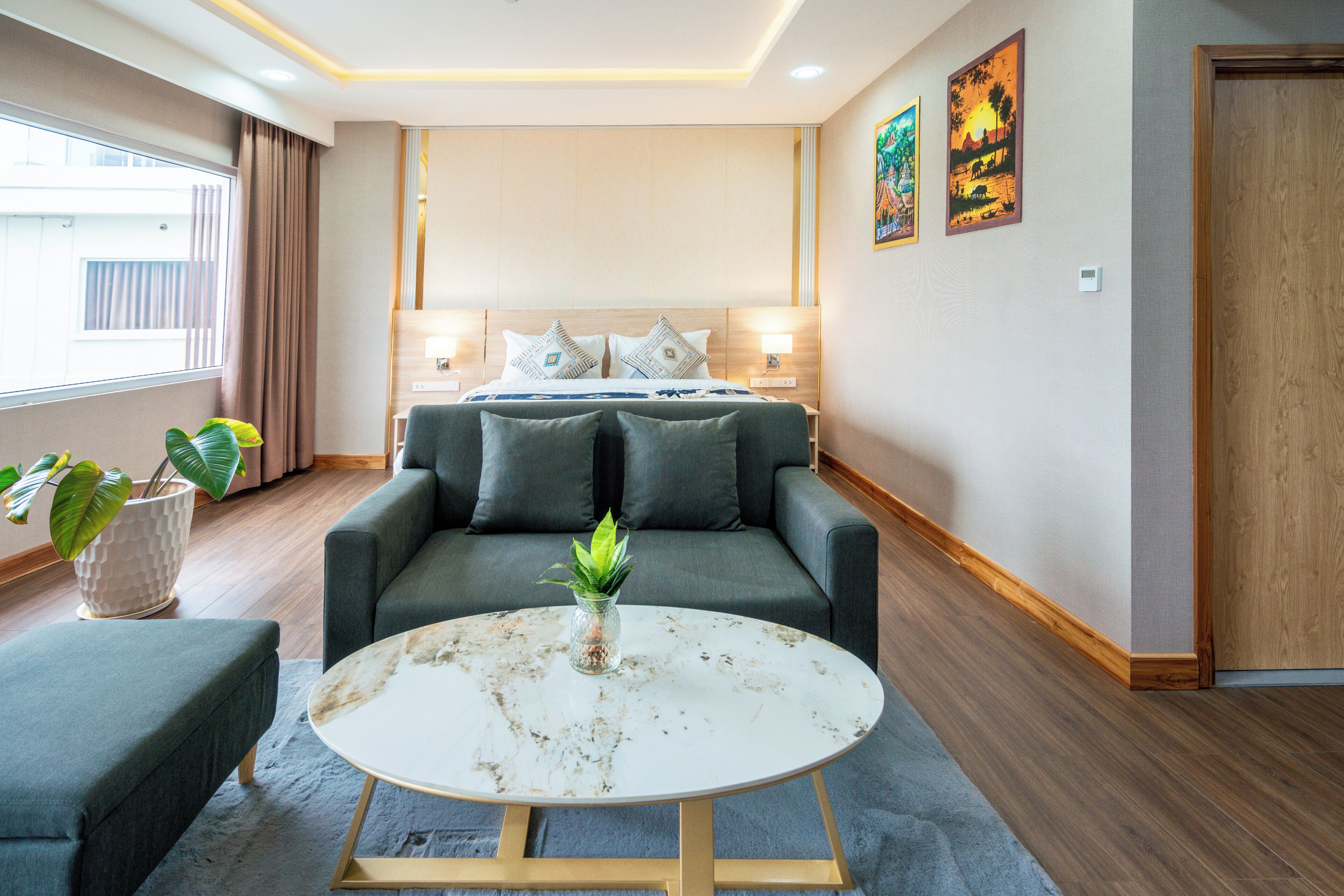 A modern hotel room with a bed, a sofa, a coffee table, and a potted plant.