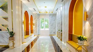 Un hall d’entrée luxueux, doté d’un sol en marbre, de touches dorées et d’un espace salon central offrant une vue sur la verdure.