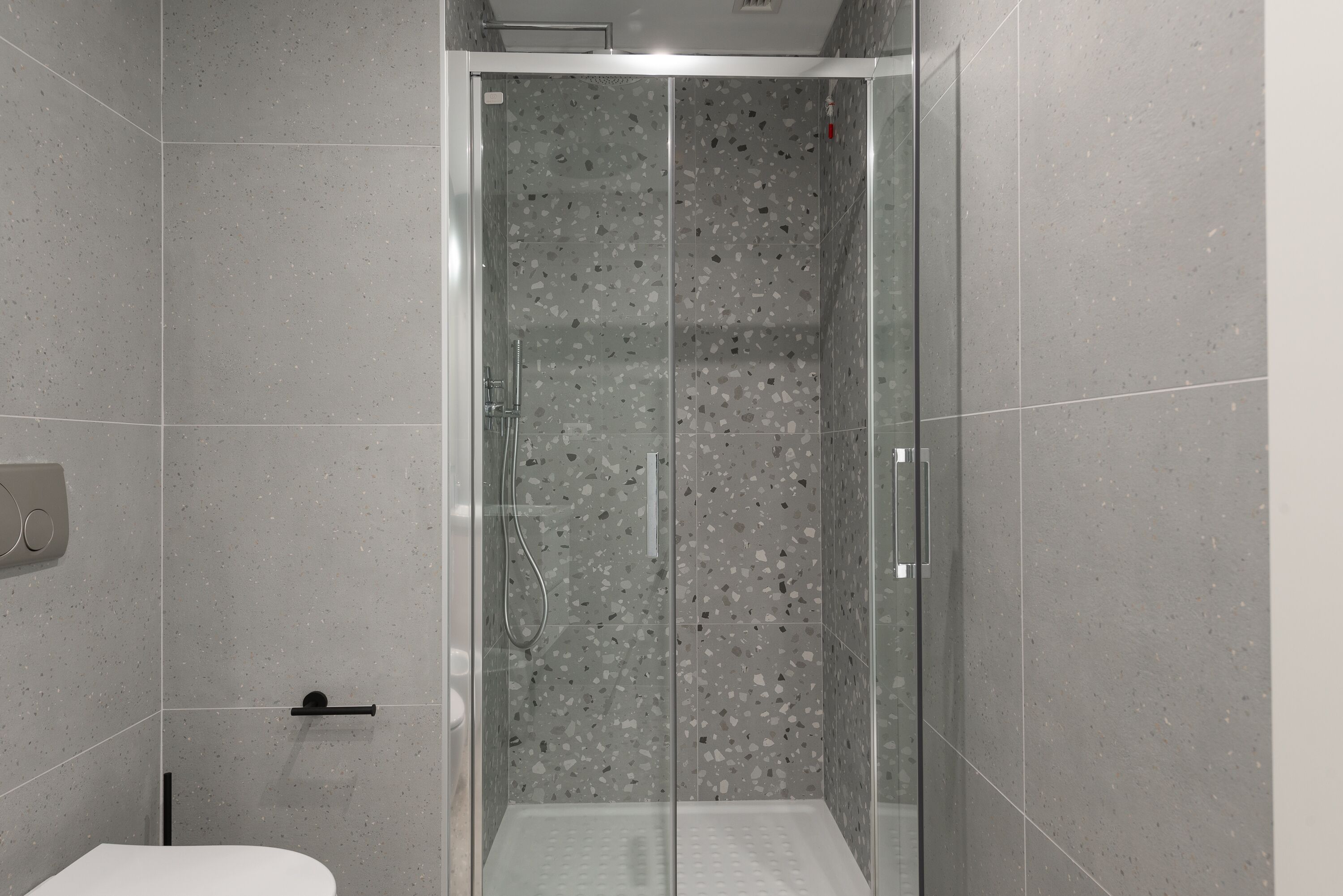A modern bathroom with a glass-enclosed shower, a toilet, and a hand dryer.