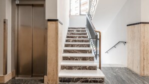 Un ascensor moderno y una escalera de mármol con barandillas de metal.