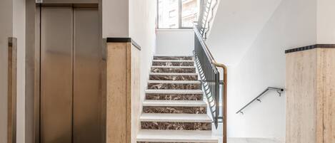 A modern elevator and a marble staircase with metal railings.