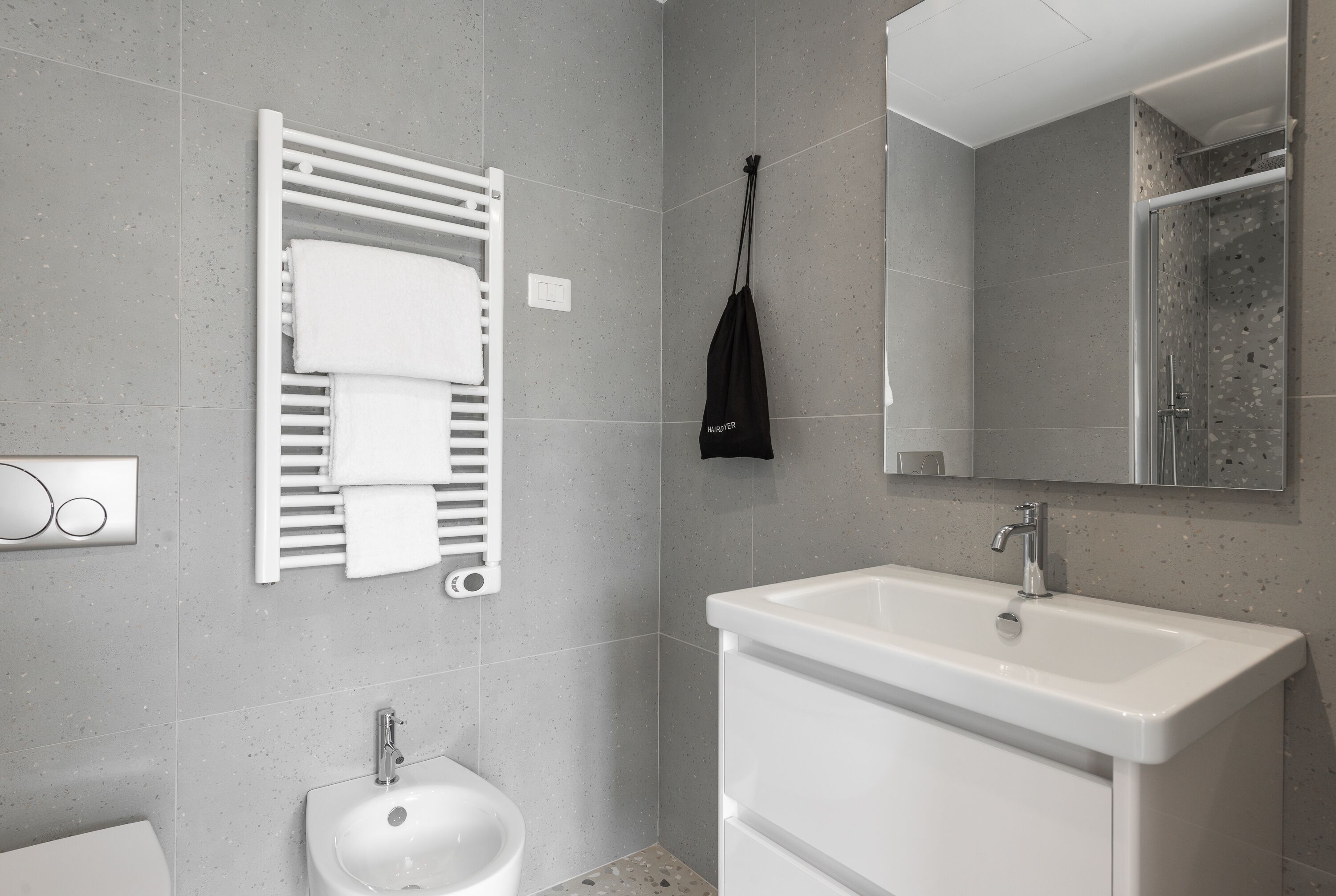 A modern bathroom with a white sink, a towel rack with folded towels, a handheld showerhead, and a mirror above the sink.