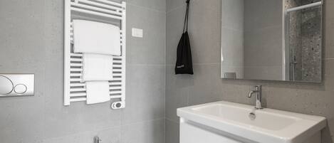 A modern bathroom with a white sink, a towel rack with folded towels, a handheld showerhead, and a mirror above the sink.