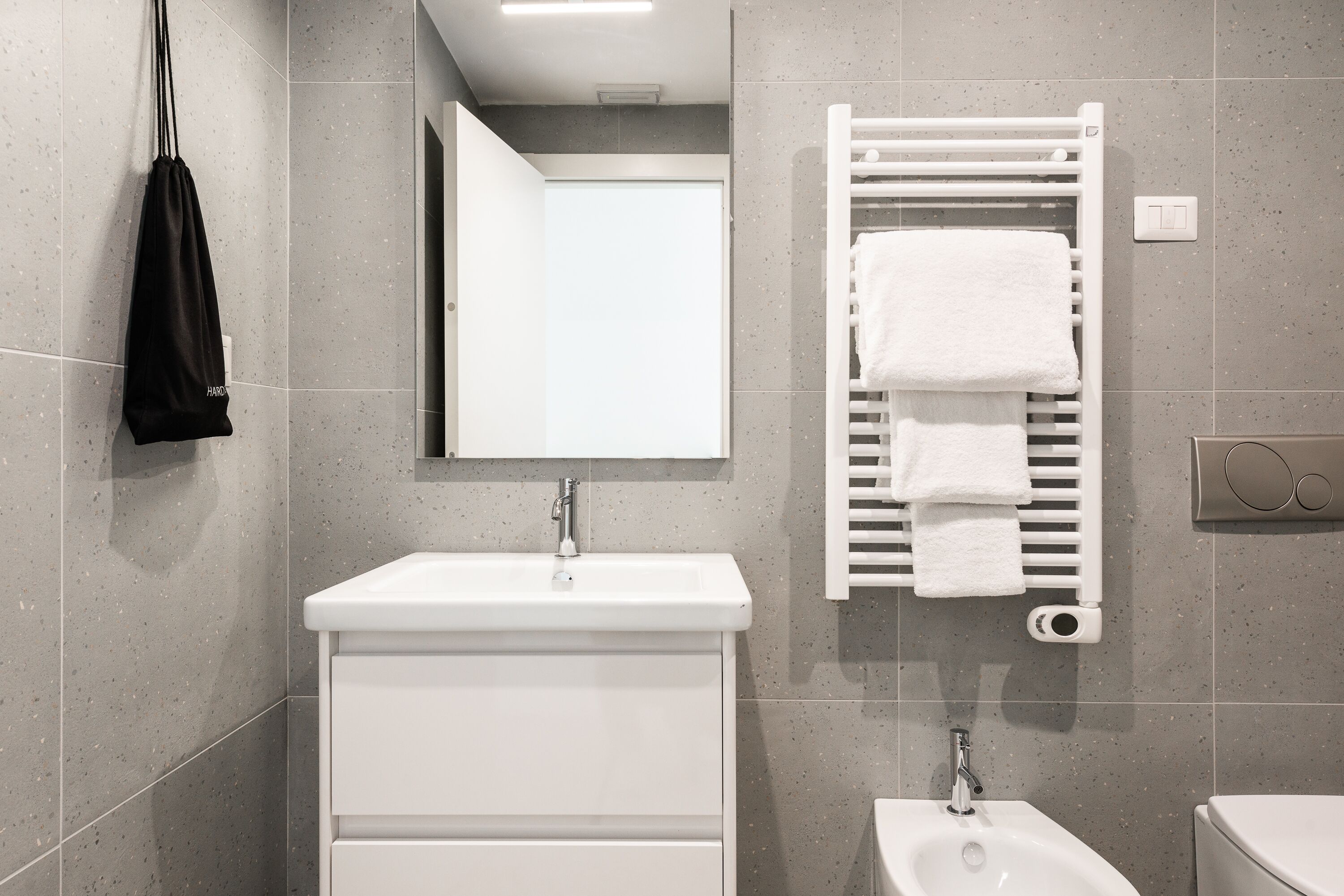 Ein modernes Badezimmer mit einem weißen Waschbecken, Spiegel und Handtuchhalter.