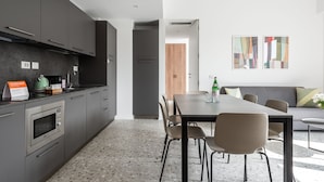 Una cocina moderna con gabinetes grises, horno empotrado y comedor con mesa y sillas.